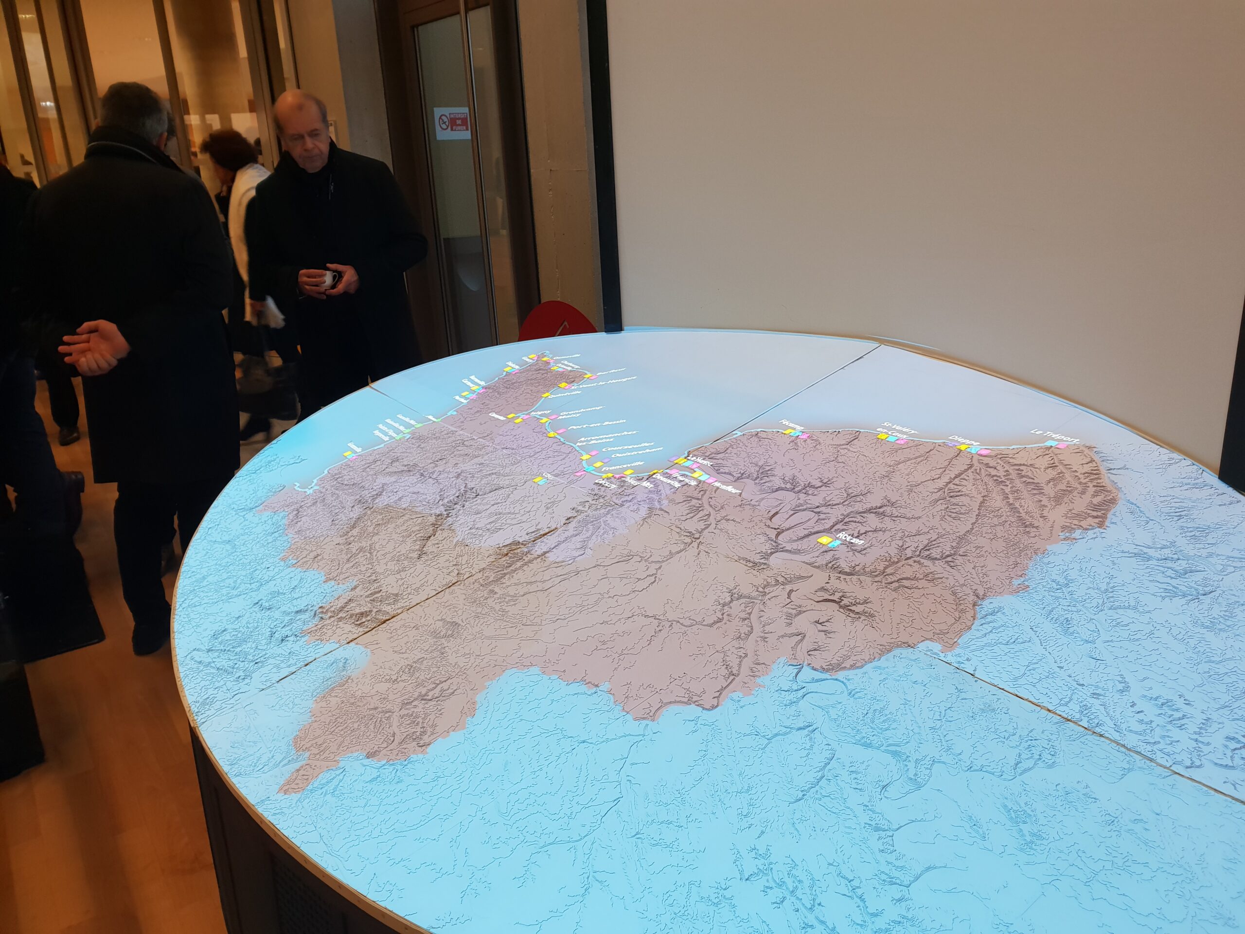 Sur la photo, deux mains sont en train de coller les pièces de la maquette NormanDisplay sur le plateau topographique